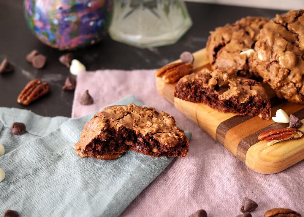 Chocolate Bliss Cookie broken to show interior texture on napkins in front of a serving board with more cookies.